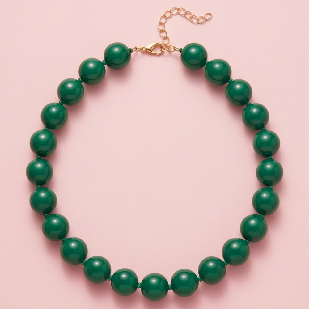 A beaded necklace made of glossy dark green round beads with a gold-tone lobster clasp and extender chain, displayed on a solid light pink background.
